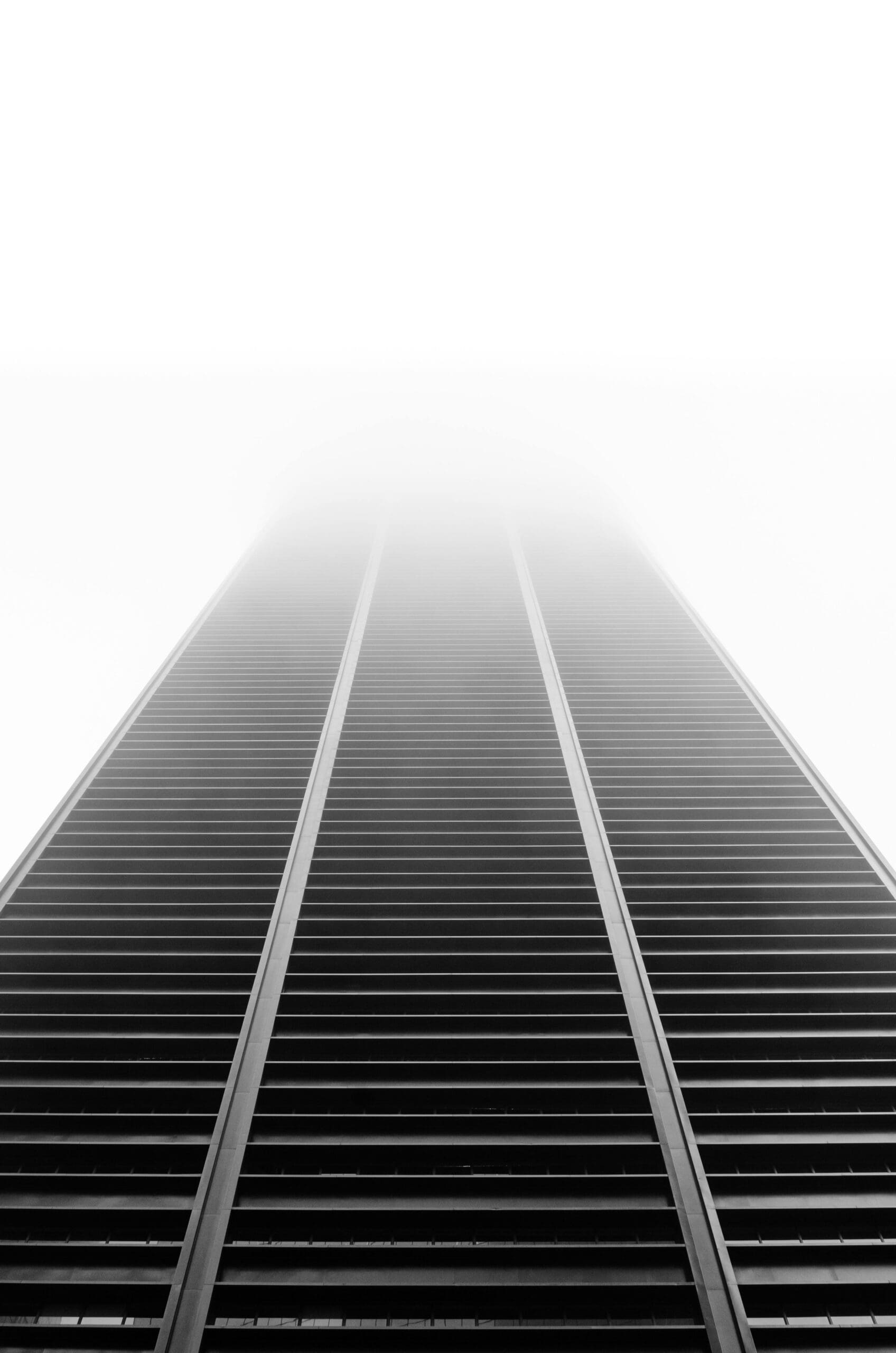 Low-angle black-and-white view of a modern building rising into fog.